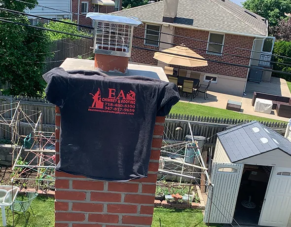 Outdoor photo of a brick chimney with a black company-branded T-shirt hanging over it showing ‘EAP’ logo during chimney cleaning service.