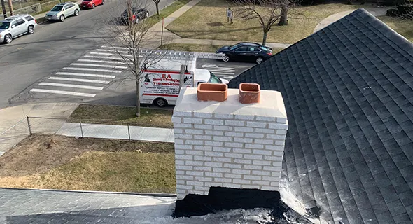 Top view of a brick chimney with metal flashing integrated into asphalt shingle roof in Manhattan, NY.