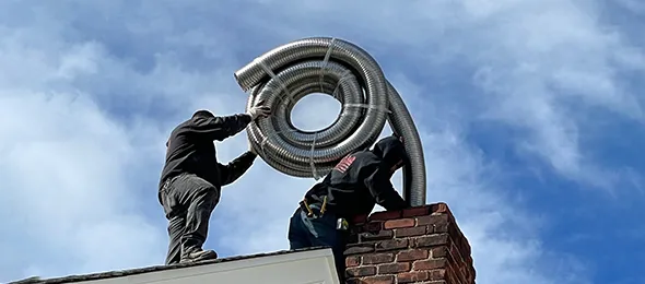 Technician holding metal chimney flue liner against blue sky during professional flue liner repair in New York City.